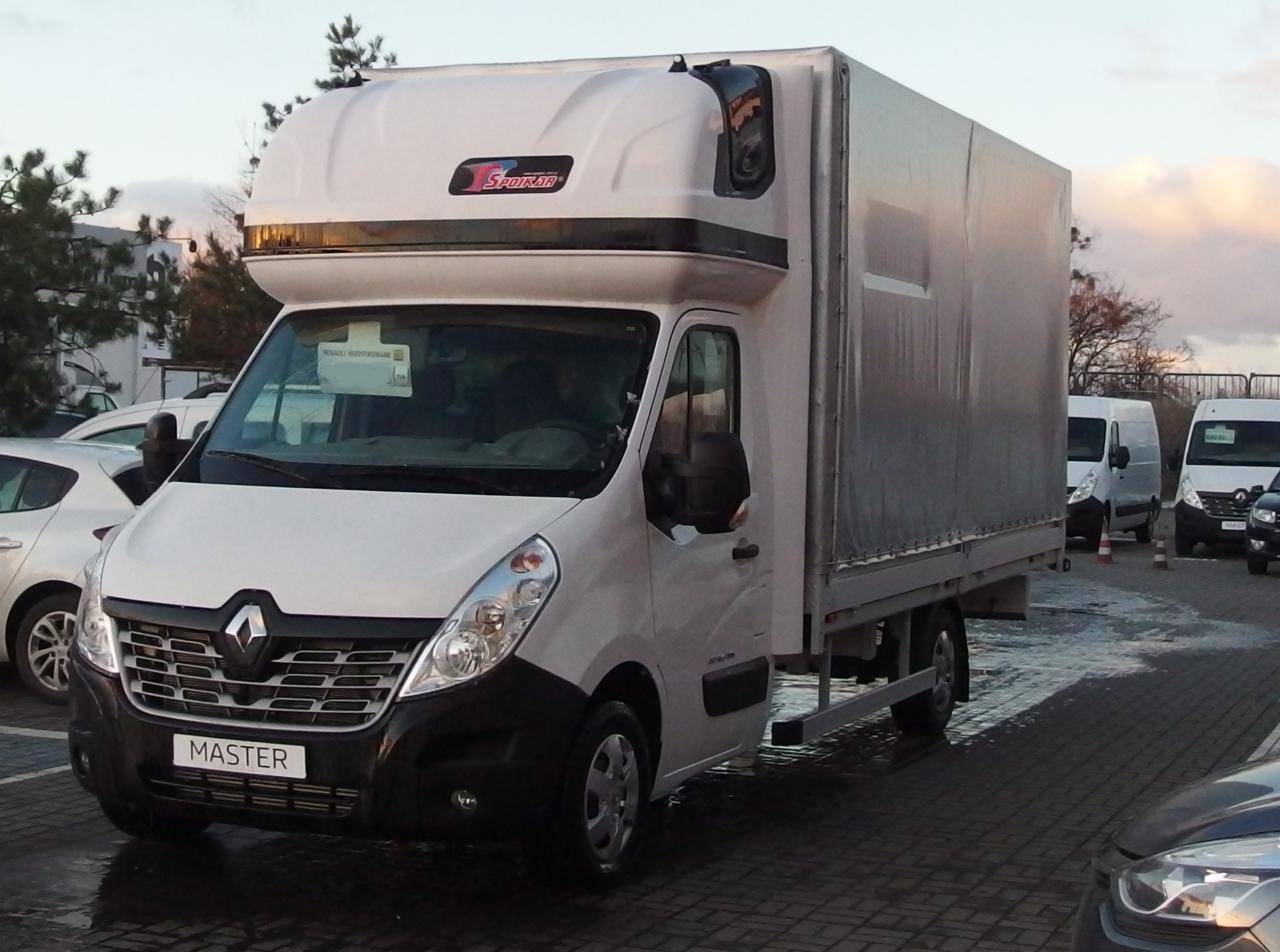 Biały Renault Master z plandeką i zabudową kabiny Storm na parkingu, widoczne inne busy w tle.