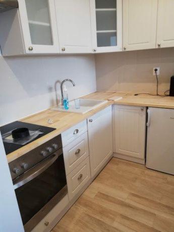 Jasna, klasyczna kuchnia z białymi szafkami z przeszklonymi górnymi frontami, drewnianym blatem, płytą indukcyjną i piekarnikiem w zabudowie, oraz małą lodówką.