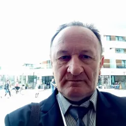 Portret mężczyzny w garniturze na tle nowoczesnego budynku i placu miejskiego z fontanną. Ujęcie z dołu.