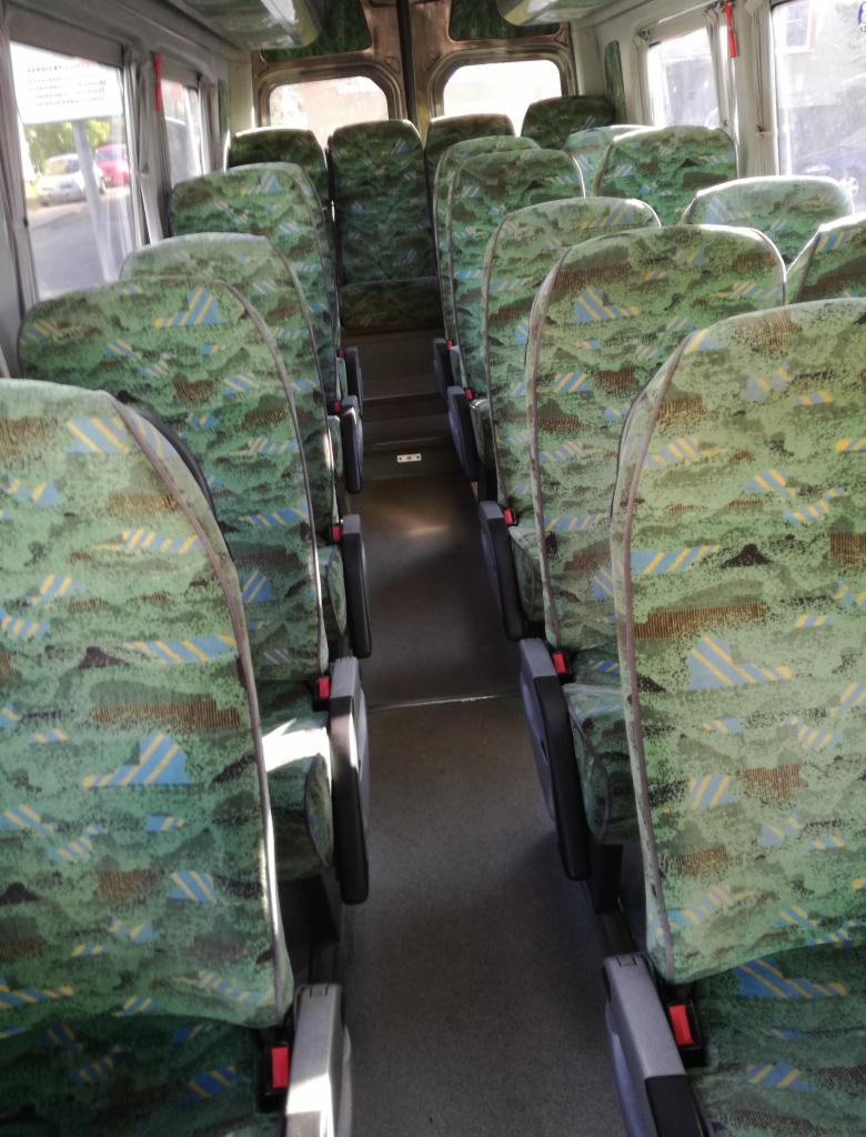 Wnętrze autobusu z rzędami zielonych foteli w abstrakcyjny wzór, widok z przodu pojazdu.