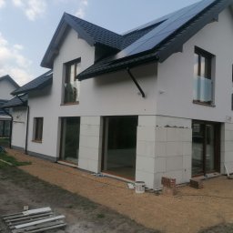 Przeszon - Nowoczesny dom jednorodzinny w trakcie wykończenia elewacji, widoczne panele słoneczne na dachu, okna z balustradami i fragmenty nieotynkowanej ściany z bloczków.