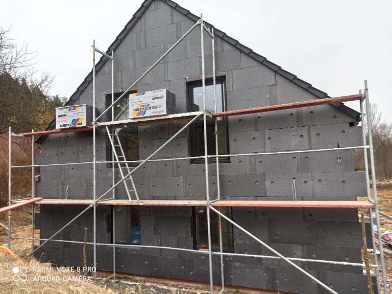 Dom jednorodzinny w trakcie ocieplania elewacji styropianem grafitowym, widoczne rusztowanie i paczki materiału izolacyjnego Austrotherm na podeście.