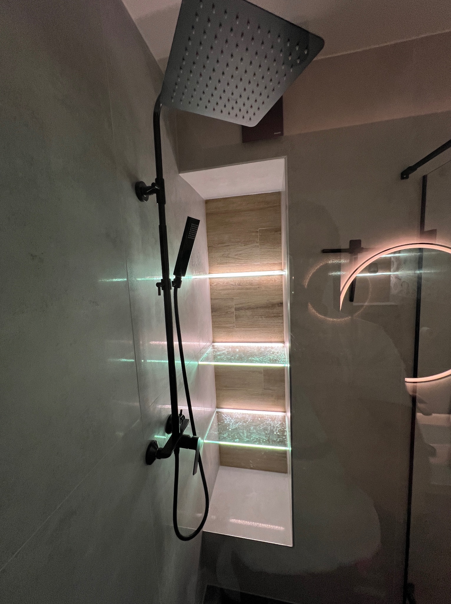 Nowoczesna kabina prysznicowa z czarną armaturą i podświetlanymi półkami wnękowymi. Minimalistyczny design, szklane elementy i subtelne oświetlenie tworzą elegancką przestrzeń kąpielową.