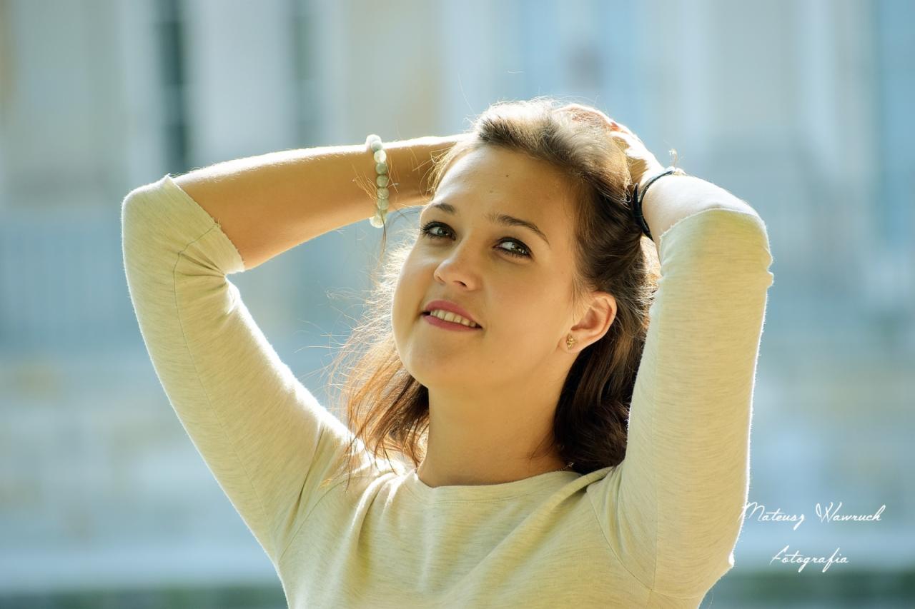 Portret młodej kobiety z włosami upiętymi do góry, uśmiechająca się i patrząca w górę, z bransoletką na ręce i widocznym znakiem wodnym fotografa w prawym dolnym rogu.