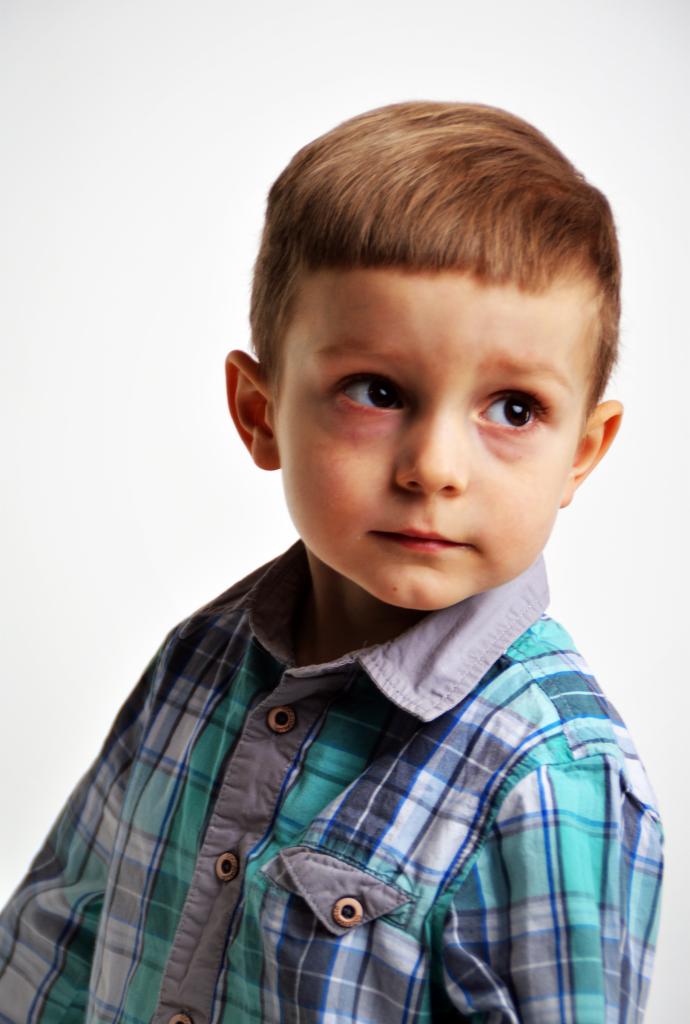 Portret chłopca w koszuli w kratę z poważnym wyrazem twarzy, spoglądającego w bok na jasnym tle.