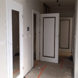 Berlin-Technik Łukasz Berliński - Wnętrze w trakcie remontu z widocznymi białymi drzwiami z przeszkleniami i bez, zabezpieczona podłoga folią malarską. Widok na kilka pomieszczeń.