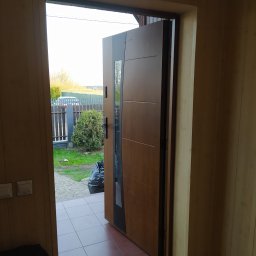 Berlin-Technik Łukasz Berliński - Otwarta, nowoczesna, drewniana brama wejściowa z czarnymi akcentami, widok z wnętrza domu na zewnątrz, z widocznym fragmentem podwórka i ogrodzenia.