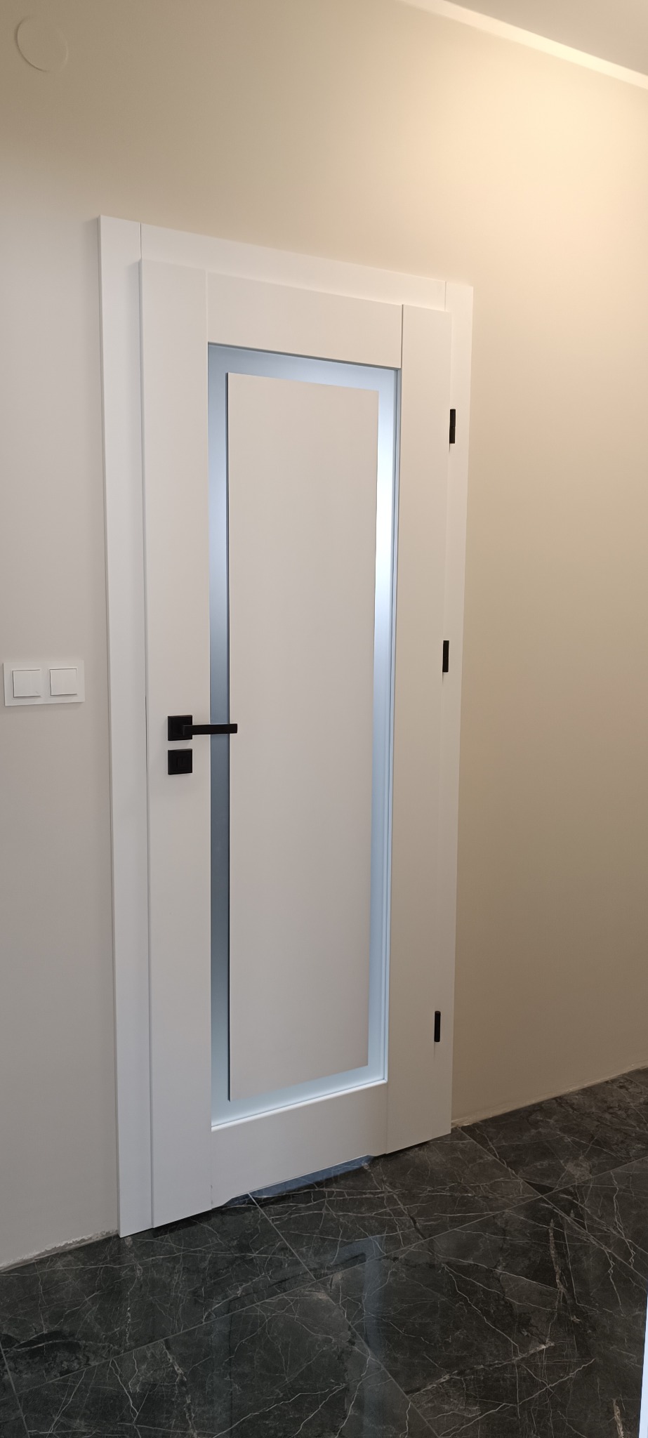 Białe, nowoczesne skrzydło z czarną klamką, zamontowane w Makowie Mazowieckim. Drzwi z przeszkleniem, minimalistyczny design, widoczne zawiasy.