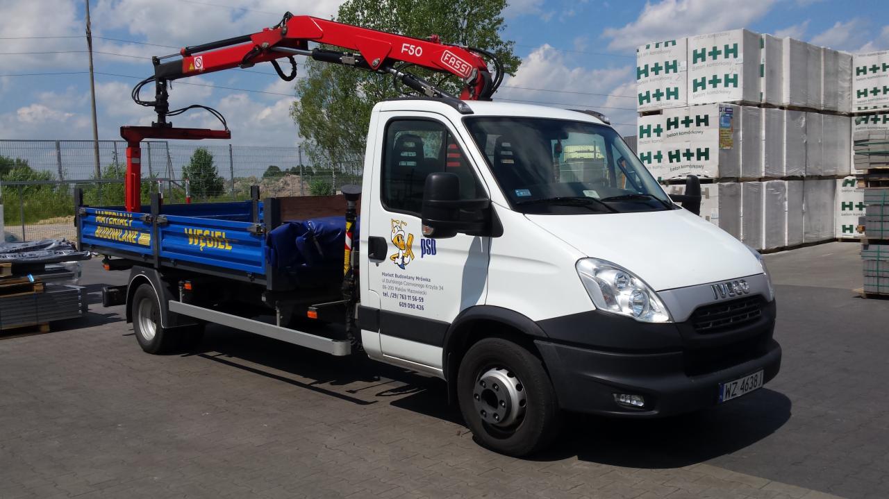 Samochód dostawczy z dźwigiem HDS firmy z Makowa Mazowieckiego, załadowany materiałami budowlanymi H+H. Widoczny logotyp firmy na drzwiach.