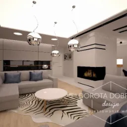 Nowoczesny salon z szarą sofą narożną, okrągłym białym stolikiem kawowym na dywanie w zebrę, kominkiem z czarną obudową i trzema wiszącymi lampami w kształcie kul, oświetleniem sufitowym oraz logo...