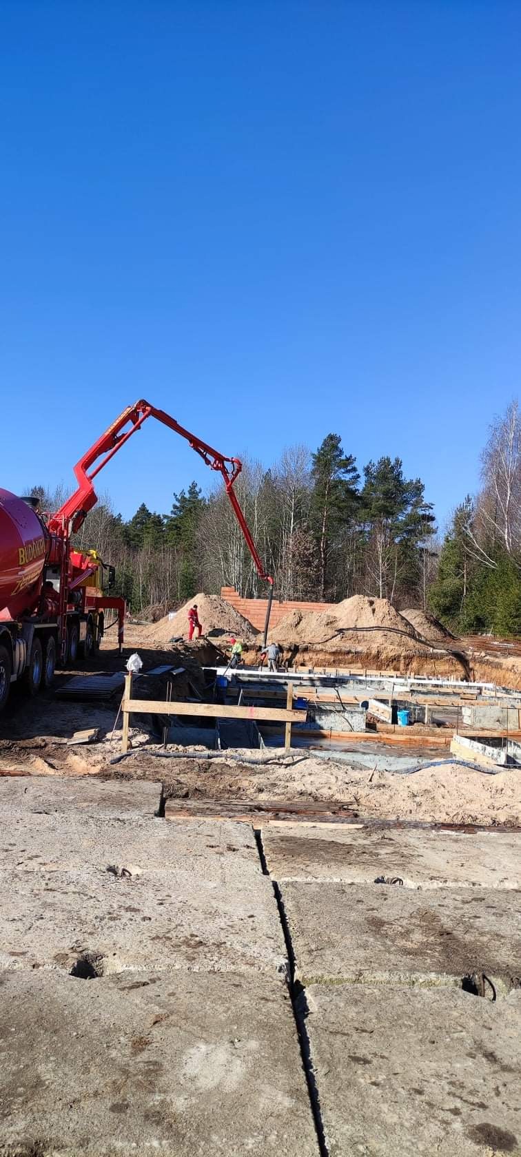 Wylewanie betonu na fundamenty domu murowanego za pomocą pompy do betonu z widocznym napisem 'BUDOWN'