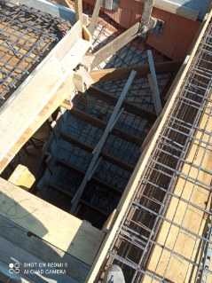 Wykopany otwór w stropie budynku, prawdopodobnie przygotowywany pod schody, widoczne zbrojenia i drewniane szalunki.