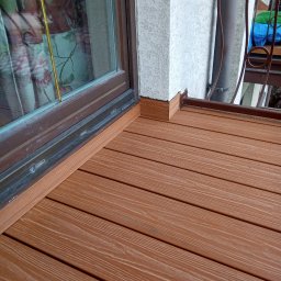 Oleksandr Kachkar GREENINDI - Wykończony taras z desek kompozytowych w odcieniach brązu, widoczny przy oknie i narożniku budynku. Detal łączenia desek z elewacją i ramą okienną.