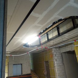 Oleksandr Kachkar GREENINDI - Montaż sufitu podwieszanego z płyt kartonowo-gipsowych, widoczne profile, instalacja elektryczna i izolacja ścian wełną mineralną w trakcie prac wykończeniowych.