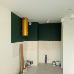 Oleksandr Kachkar GREENINDI - Wnętrze w trakcie prac: ściany pomalowane na biało i ciemnozielono, fragment ściany z tapetą w liście, puszki z farbą na podłodze, drabina z pracownikiem, widoczne instalacje hydrauliczne...