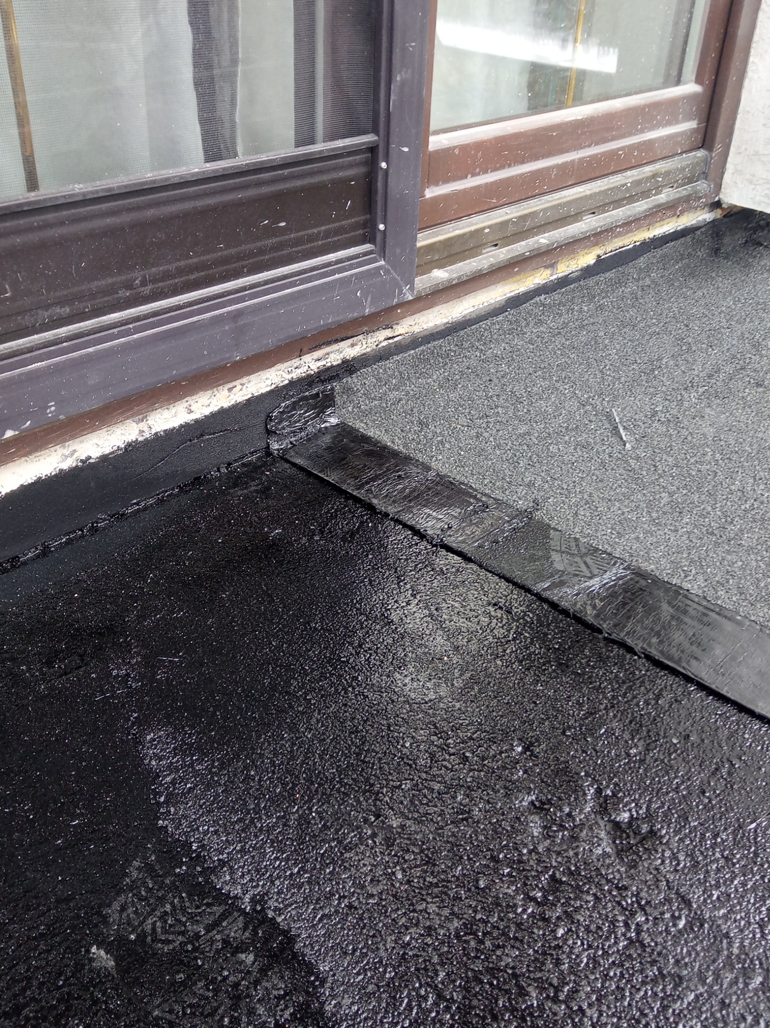 Hydroizolacja balkonu przy oknie, widoczna czarna masa bitumiczna i szary materiał wykończeniowy. Detal łączenia warstw.