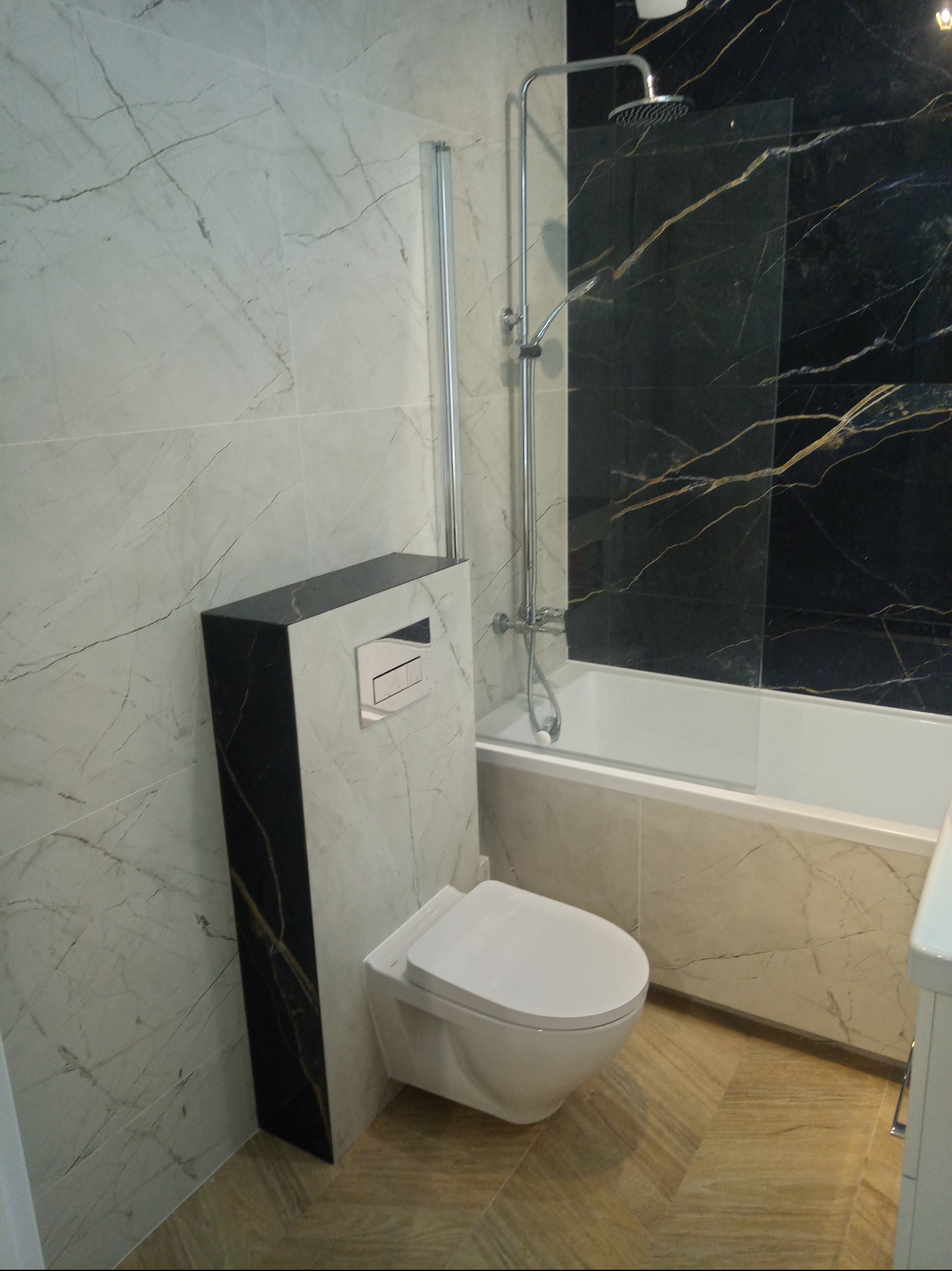 Nowoczesna łazienka z marmurowymi płytkami, wiszącą toaletą z czarnym panelem i kabiną prysznicową ze złotymi żyłami. Ukończona aranżacja wnętrza.