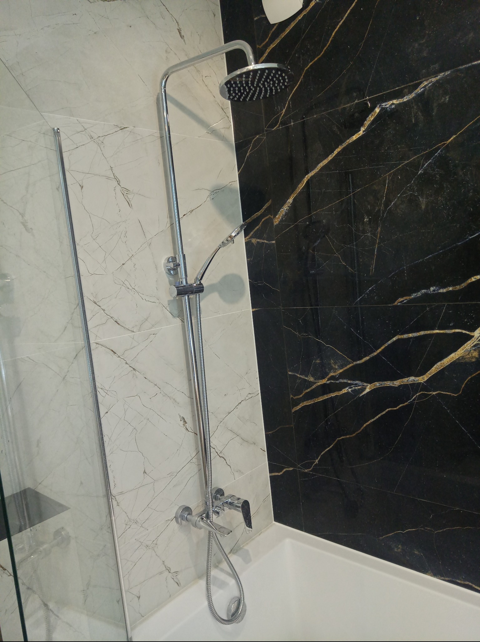 Nowoczesna łazienka z kabiną prysznicową, wykończona płytkami imitującymi marmur w odcieniach bieli i czerni ze złotymi żyłami. Chromowana armatura.