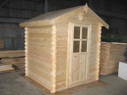 Mały domek z bali z oknem i drzwiami, prawdopodobnie domek narzędziowy lub letniskowy, wykonany w Jabłonnie. Widoczne drewniane elementy konstrukcyjne i surowe wykończenie.