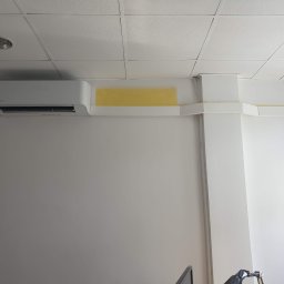 Frost Me - Biała klimatyzacja Toshiba zamontowana na ścianie w biurze, widoczne żółte taśmy zabezpieczające podczas montażu, kratka sufitowa w tle.