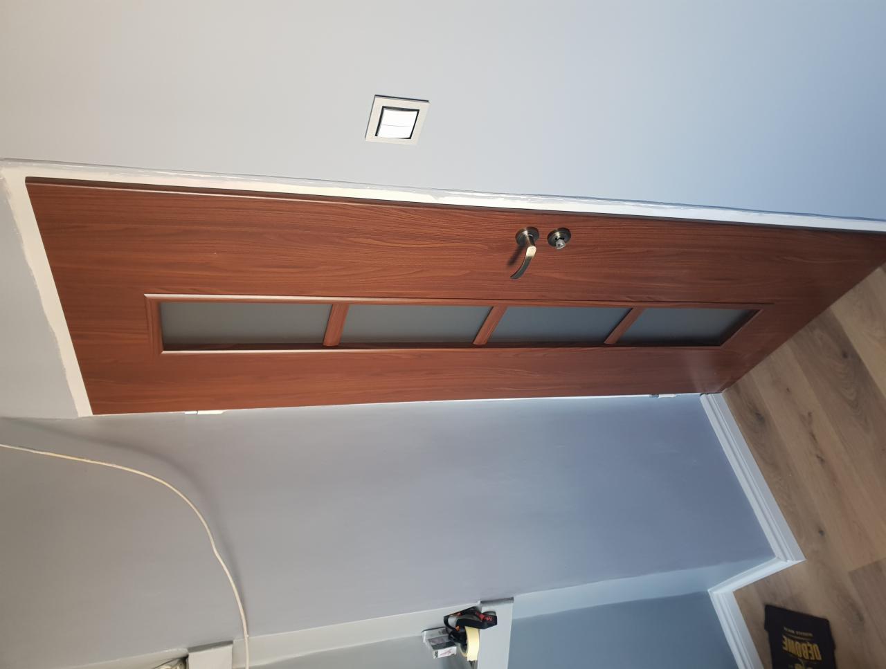 Zamontowane, drewniane drzwi wewnętrzne z trzema szybkami, widoczne świeżo pomalowane odcięcie ściany od ościeżnicy.