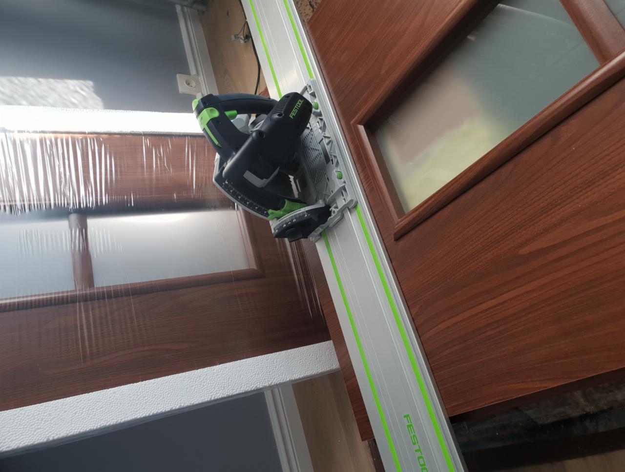 Cięcie drewnianych drzwi wewnętrznych w Warszawie za pomocą pilarki zagłębiarki Festool z szyną prowadzącą, zabezpieczonych folią ochronną.