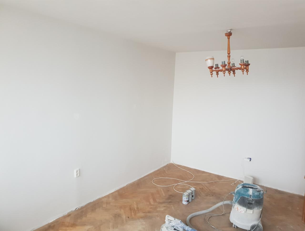 Pokój po świeżym pomalowaniu na biało, widoczny parkiet, odkurzacz przemysłowy, puszki po farbie i drewniany żyrandol.