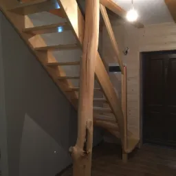 Drewniane schody z balustradą z surowego pnia drzewa, prowadzące na antresolę w domu z drewnianą boazerią.