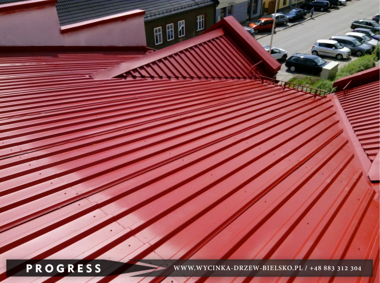 Czerwony dach z blachy trapezowej, widok z góry na budynek z ulicą i samochodami w tle.