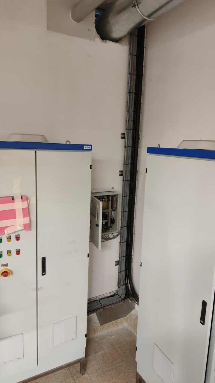 Dwie białe szafy sterownicze z widocznymi kablami i otwartą skrzynką elektryczną w Wróbliku Szlacheckim, z widocznym fragmentem instalacji wentylacyjnej pod sufitem.