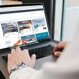 Osoba przegląda na laptopie marketplace z motywami dla stron internetowych, widoczne nazwy motywów: Stratus, Vast, Soar, Ridge, Aero, Launch, z filtrami po lewej stronie, na nadgarstku zegarek