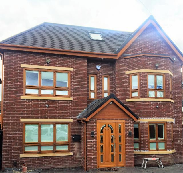 Dwupiętrowy dom z czerwonej cegły z drewnianymi oknami i drzwiami, widoczne rusztowanie przed wejściem.