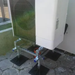 Biała jednostka zewnętrzna z logo Mitsubishi Zubadan zamontowana na metalowej konstrukcji na szarym brukowanym podłożu