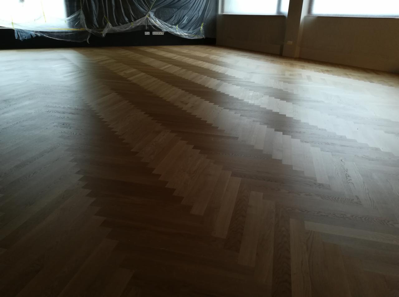 Nowa, jasna podłoga ułożona w jodełkę francuską, z widocznym zabezpieczeniem folią malarską na ścianach w tle.