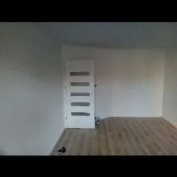 Pusty pokój po remoncie z białymi ścianami, drewnianą podłogą i białymi drzwiami z przeszkleniami; widoczne narzędzia na podłodze.