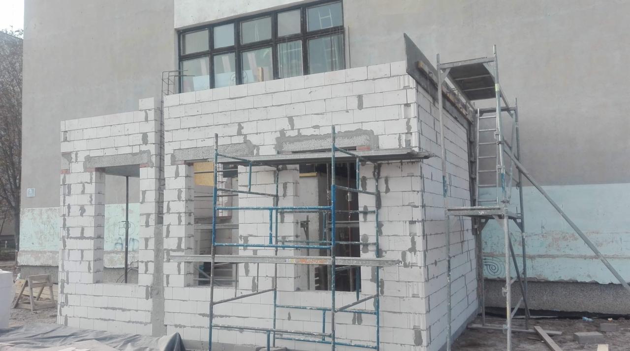 Wznoszenie ścian zewnętrznych z białych bloczków silikatowych, widoczne rusztowania i otwory okienne w surowym stanie.