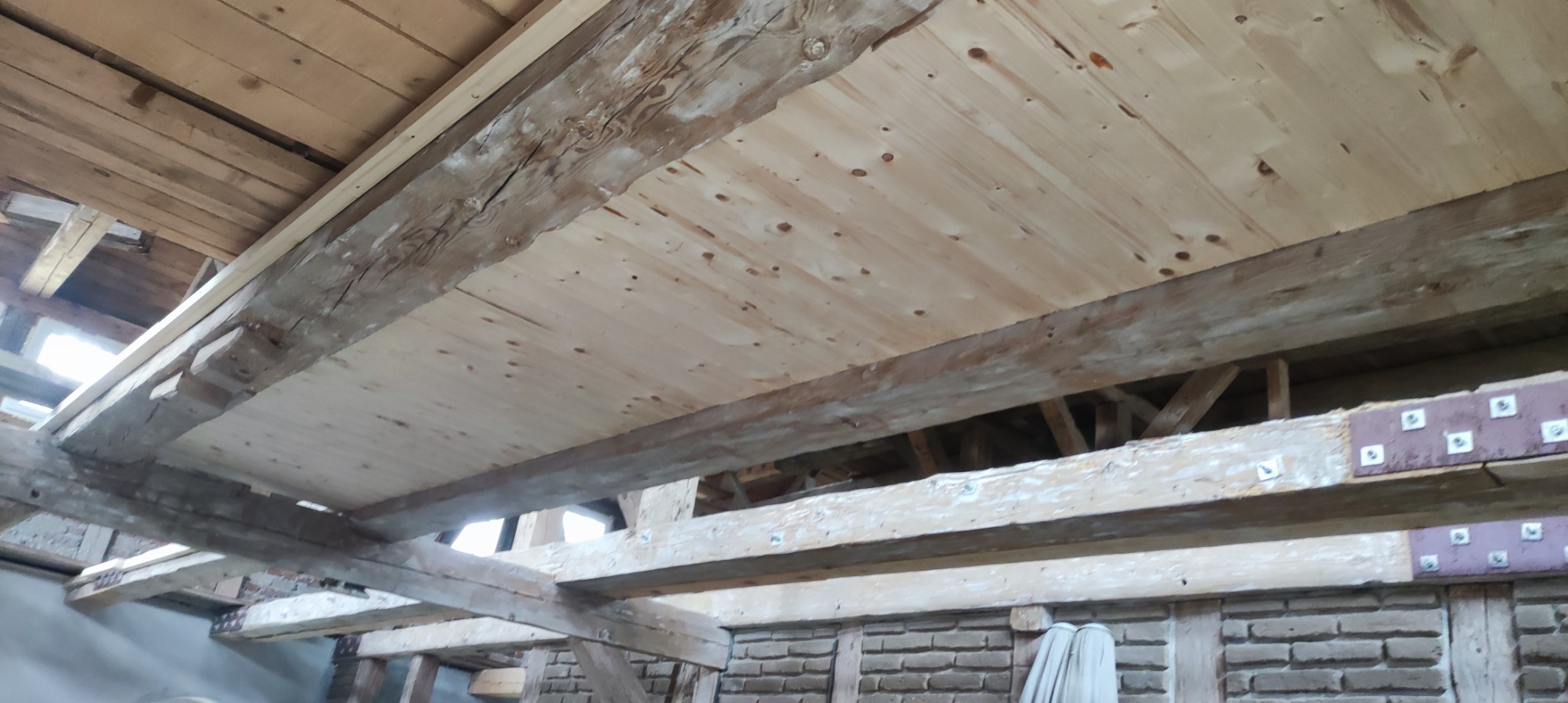 Drewniany strop z widocznymi belkami nośnymi i deskowaniem, surowe wykończenie, widok od dołu, specyfika starego budownictwa.