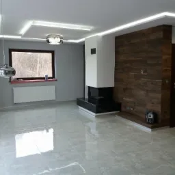 Nowoczesny salon z szarą marmurową posadzką, drewnianą ścianą z wbudowanym kominkiem, oświetleniem LED na suficie i wiszącą lampą chromowaną.