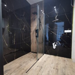 F.H.U.LUK- POL Łukasz Dereń - Nowoczesna łazienka z czarnymi płytkami imitującymi marmur ze złotymi żyłami, drewnopodobnymi płytkami podłogowymi i kabiną prysznicową typu walk-in z czarną armaturą, widoczne niedokończone prace...