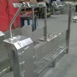 Metalowa konstrukcja z profili i blach, prawdopodobnie element linii produkcyjnej, widoczny w hali przemysłowej z wózkiem widłowym w tle.