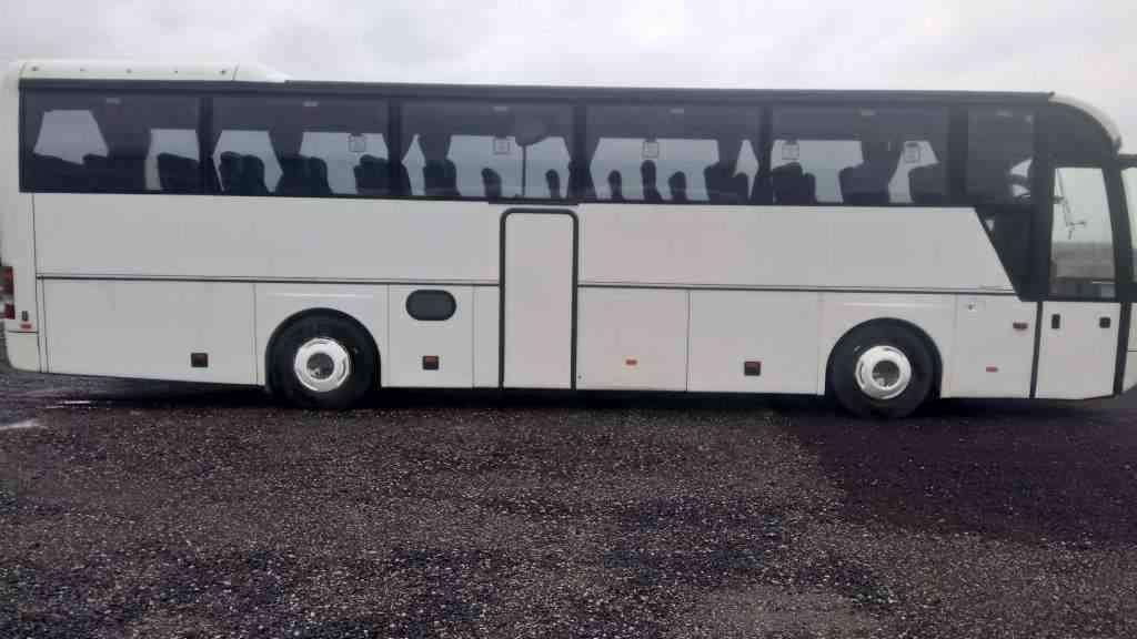 Biały autokar z otwartymi drzwiami na szarym, asfaltowym podłożu, widok z boku, lekko pochmurne niebo.