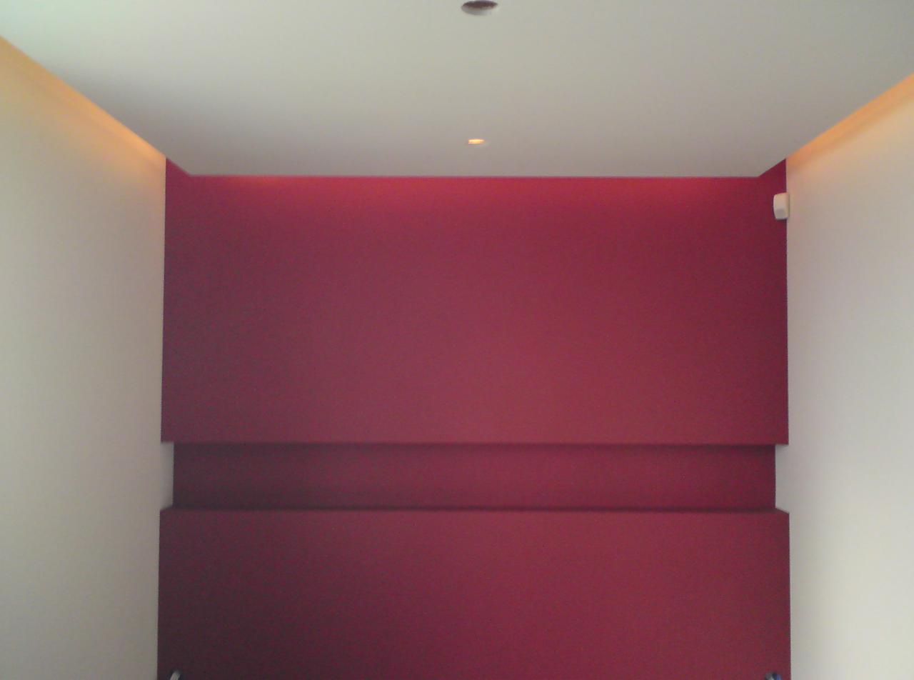 Wnętrze z bordową ścianą z poziomym, wystającym elementem dekoracyjnym, oświetleniem punktowym w suficie i białymi ścianami bocznymi.