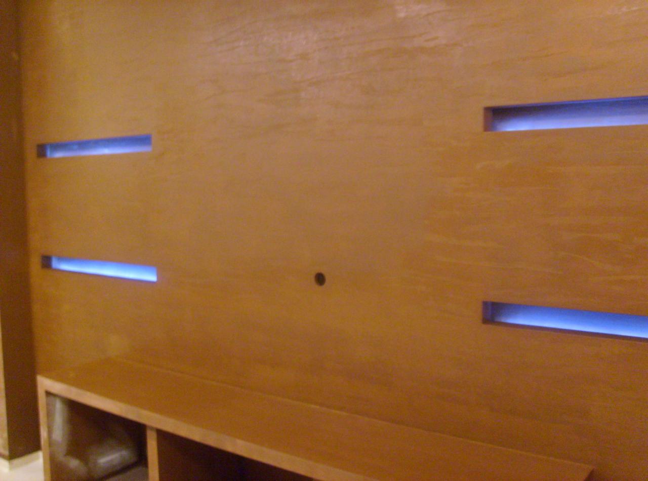 Ściana z dekoracyjną fakturą drewna i podświetlanymi, poziomymi wnękami, nad niską szafką RTV.