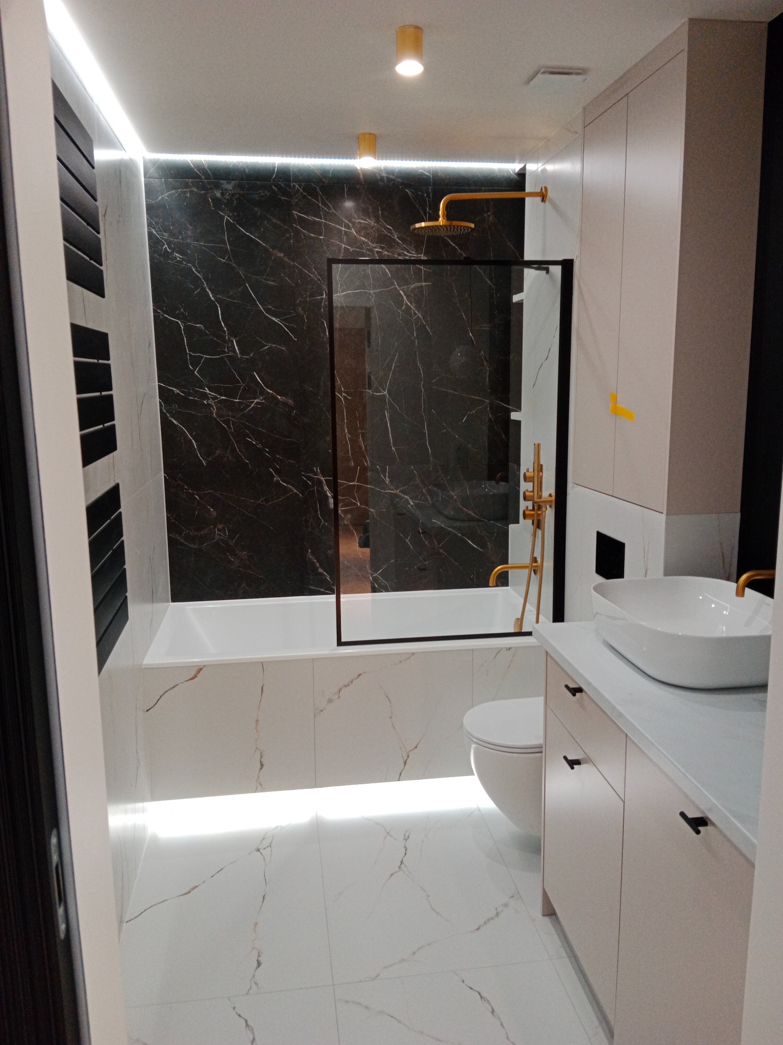 Nowoczesna łazienka z czarno-białymi marmurkowymi płytkami, złotą armaturą i podświetleniem LED
