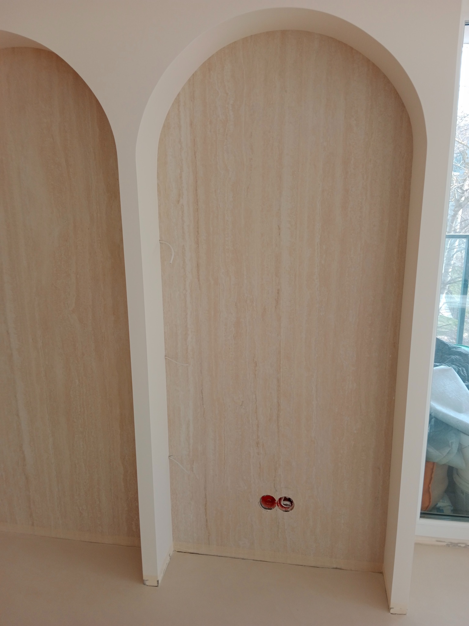 Dwie wnęki w ścianie wykończone okładziną imitującą trawertyn, z widocznymi przewodami elektrycznymi i gniazdkami, w trakcie prac wykończeniowych.