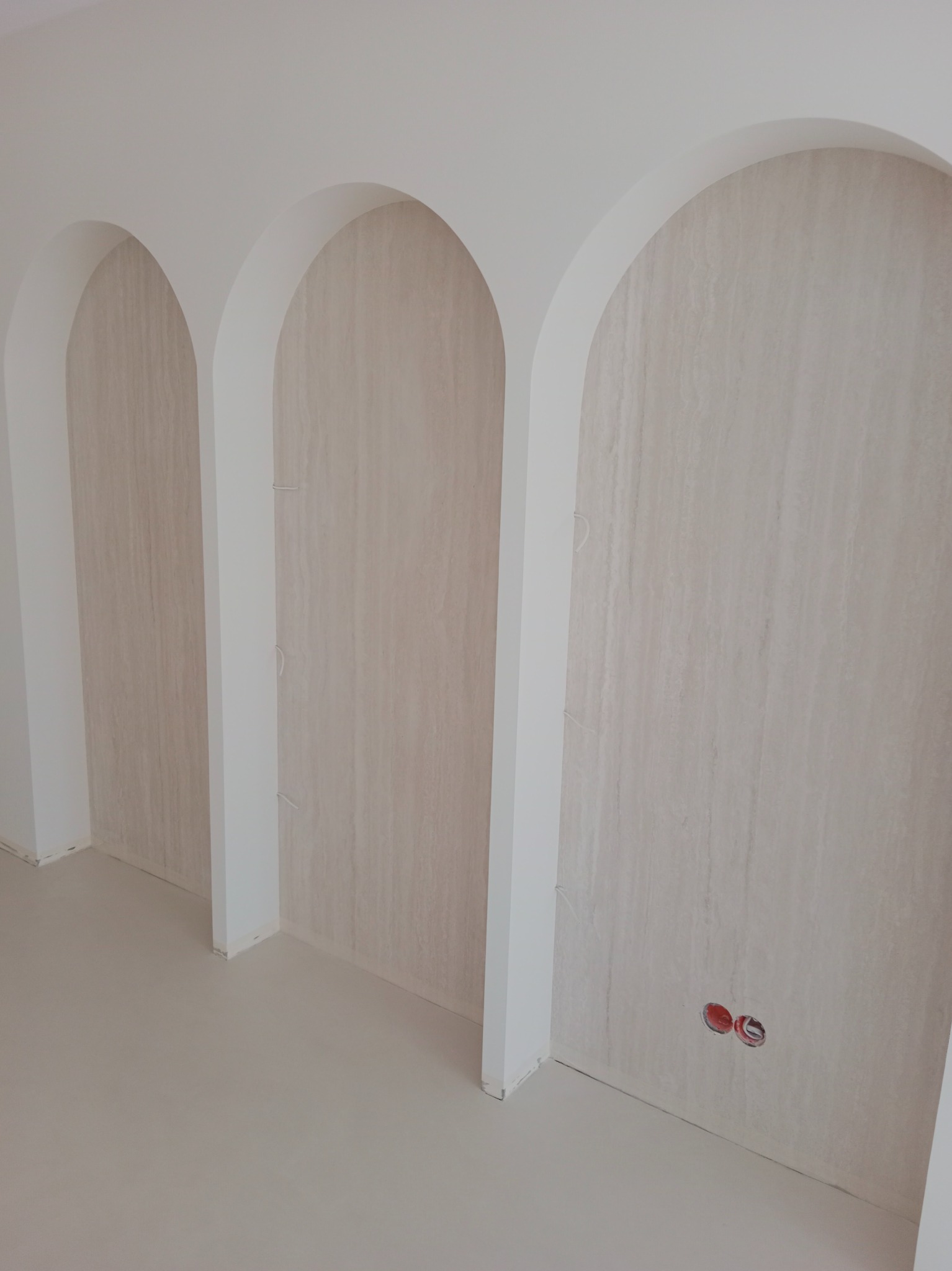 Wnęki w kształcie łuków w ścianie, wykończone tapetą o subtelnym wzorze, z widocznymi przewodami, gładka, jasna podłoga.