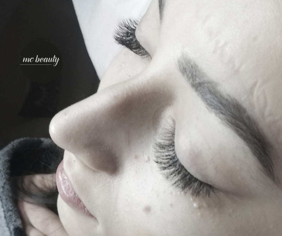 Profil twarzy kobiety po zabiegu przedłużania rzęs metodą objętościową, z widocznym logo salonu 'mc beauty' w lewym górnym rogu.