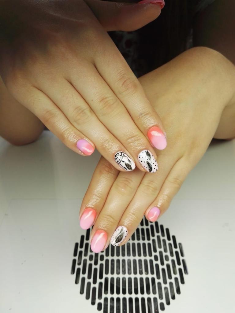 Dłonie z ombre w odcieniach różu i zdobieniami piór i łapacza snów na białym tle, widoczna kratka pochłaniacza pyłu.