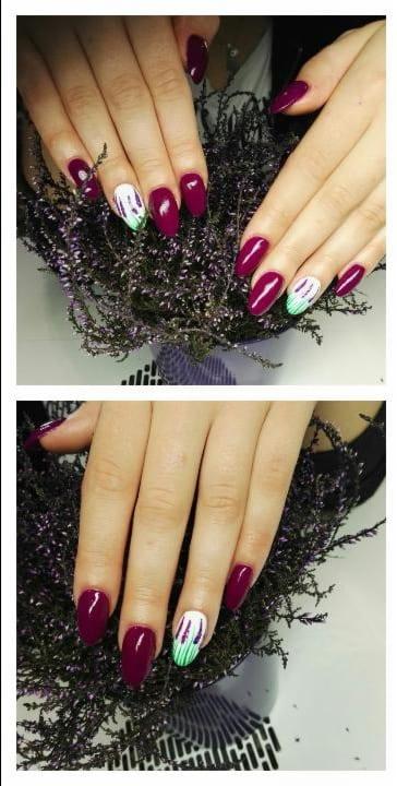 Dłonie z bordowymi paznokciami w kształcie migdała i jednym paznokciem z białym tłem i zielono-fioletowymi pociągnięciami pędzla, na tle wrzosu.