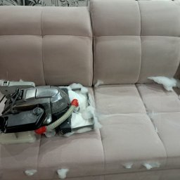 PHU MARTYNA-CZYSZCZENIE ŁÓŻEK,KANAP,NAROŻNIKÓW DYWANÓW I FOTELI KIRBY - Beżowa kanapa z widocznym fragmentem czyszczonej powierzchni i pianą. Na kanapie stoi odkurzacz piorący z widocznym zbiornikiem na wodę i wężykiem.